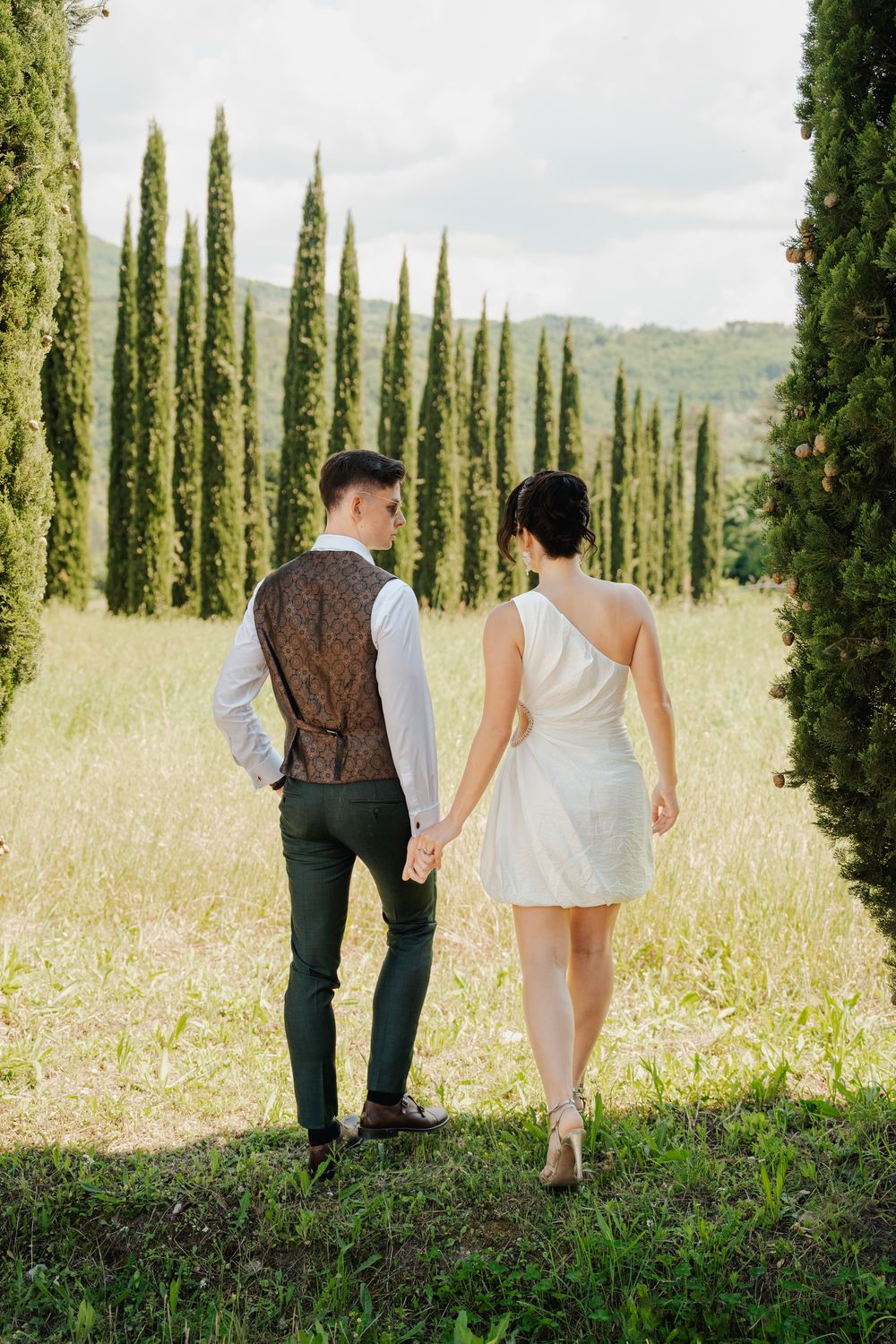 Para młoda w Toskanii idzie wśród cyprysów, naturalne światło, fine art wedding photography za granicą.