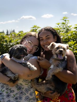 A woman shows affection to a small dog while outdoors on a sunny day.