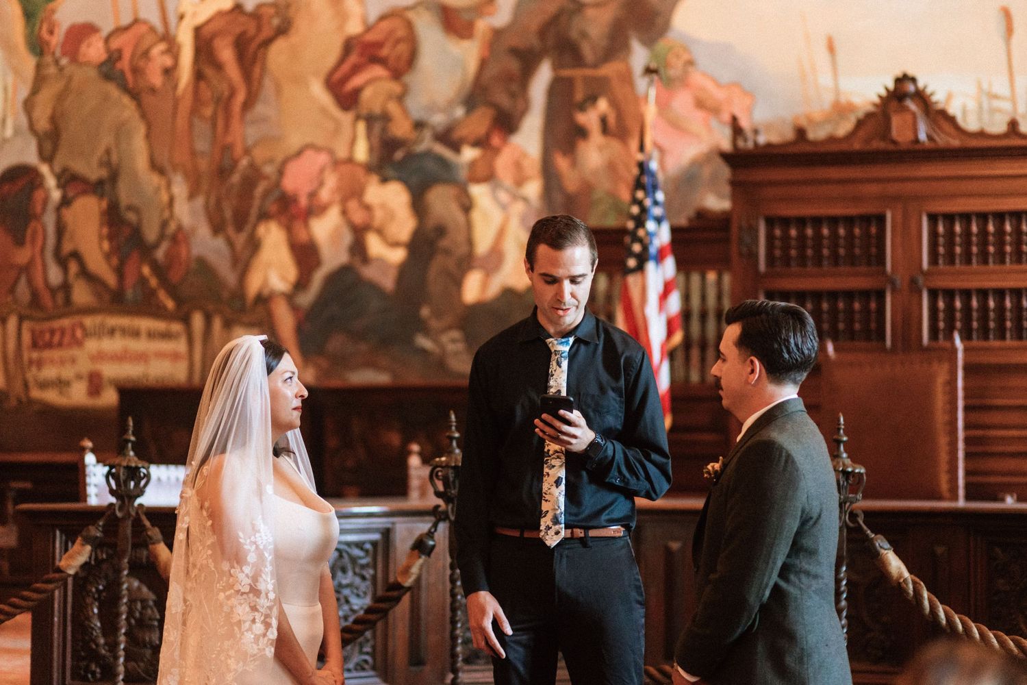 A bride and groom stand in the mural room at the Santa Barbara courthouse for their wedding ceremony