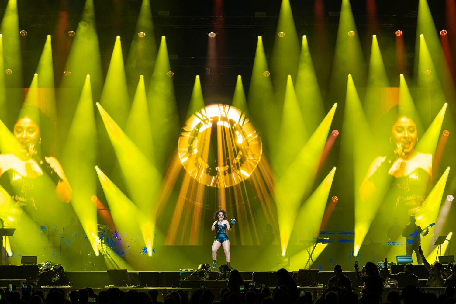 Concert stage performance with dramatic yellow spotlights and a glowing circular halo effect in front of a dark backdrop.