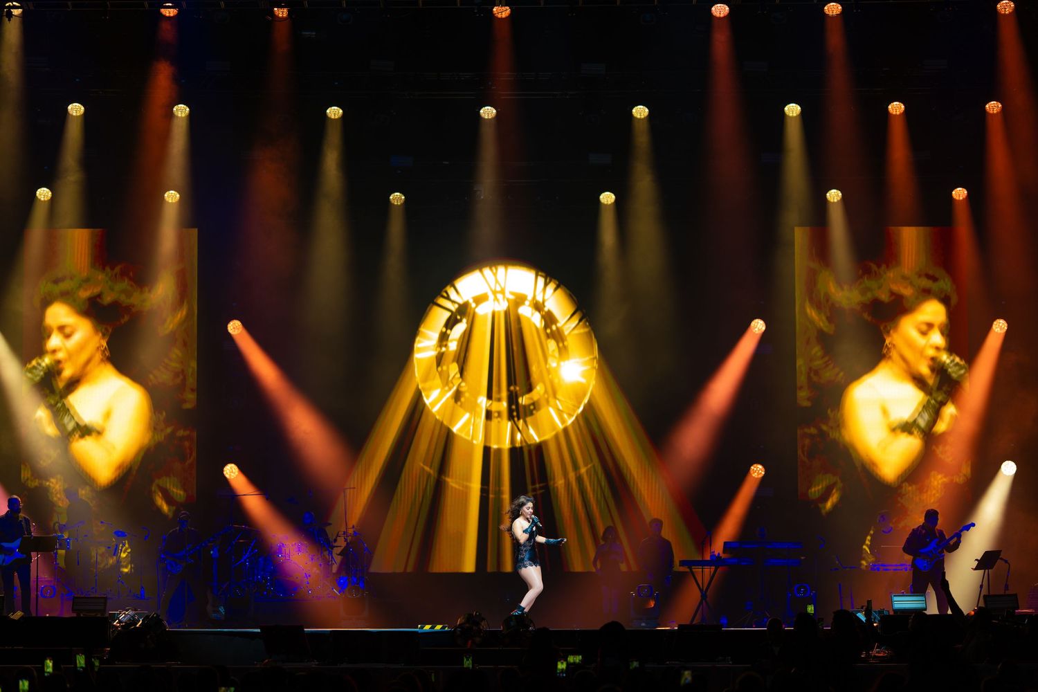 Concert stage illuminated with dramatic yellow and purple spotlights creating an atmospheric lighting display.