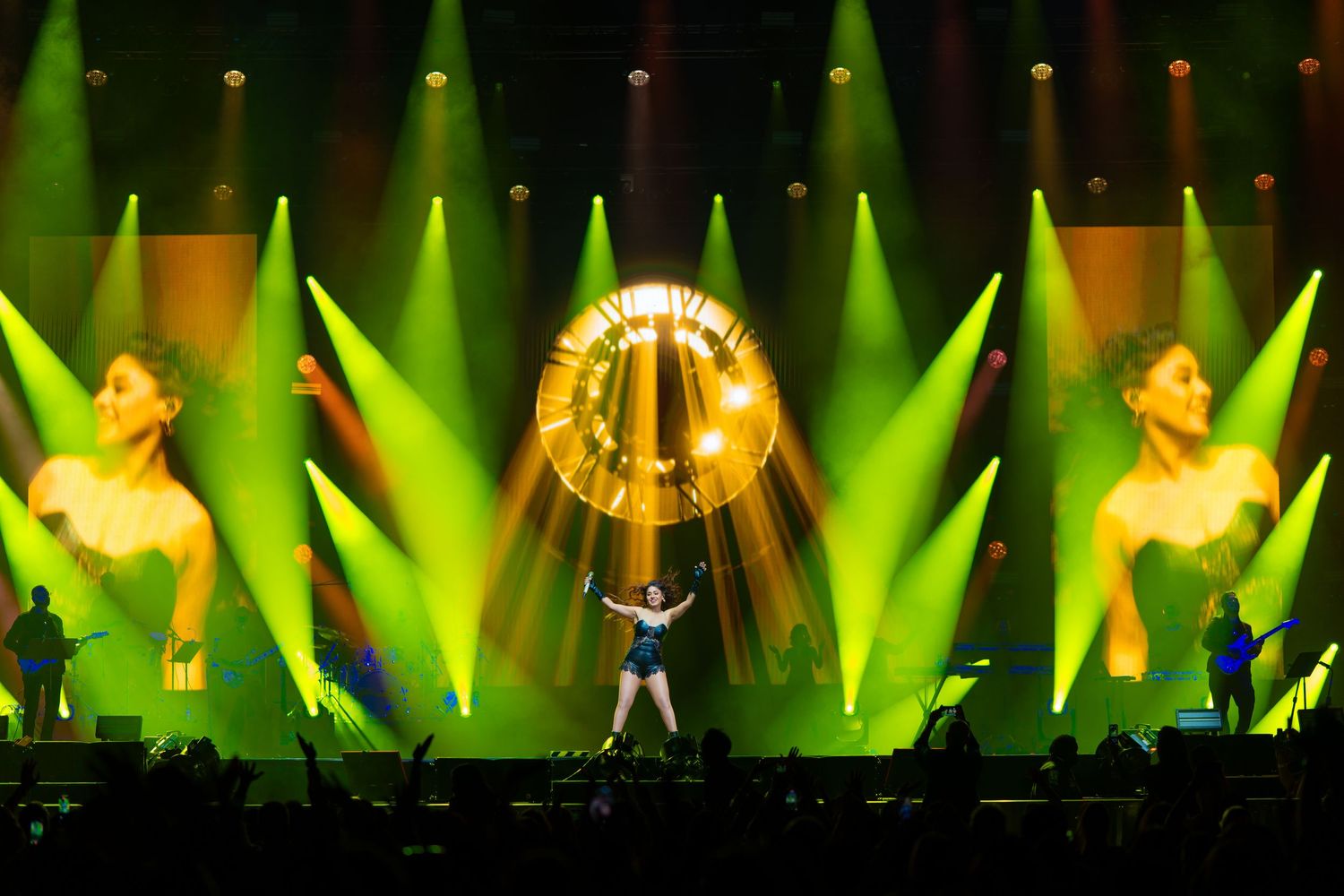 Dynamic concert stage performance with bright yellow-green lighting and large illuminated circular display in background.