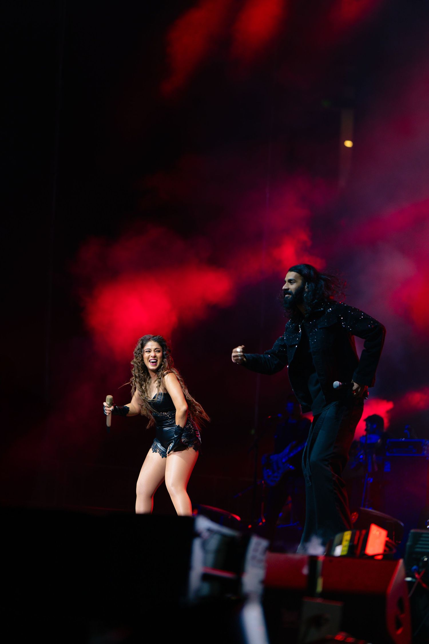 Performers on stage in dramatic silhouettes against moody red and blue lighting during an energetic concert performance.