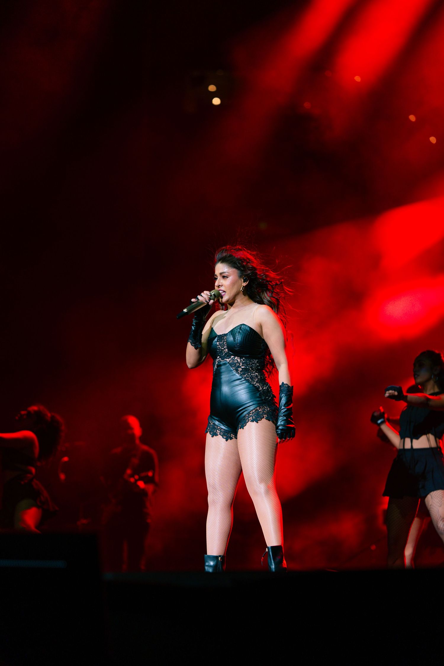 A performer sings on stage in a black costume under dramatic red lighting during a concert performance.