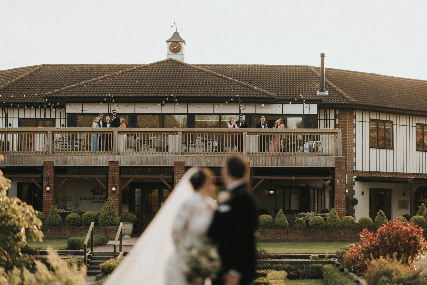 Wedding couple stand on the lawn and look behind them at Laceby Manor. Image taken by Grimsby photographers.