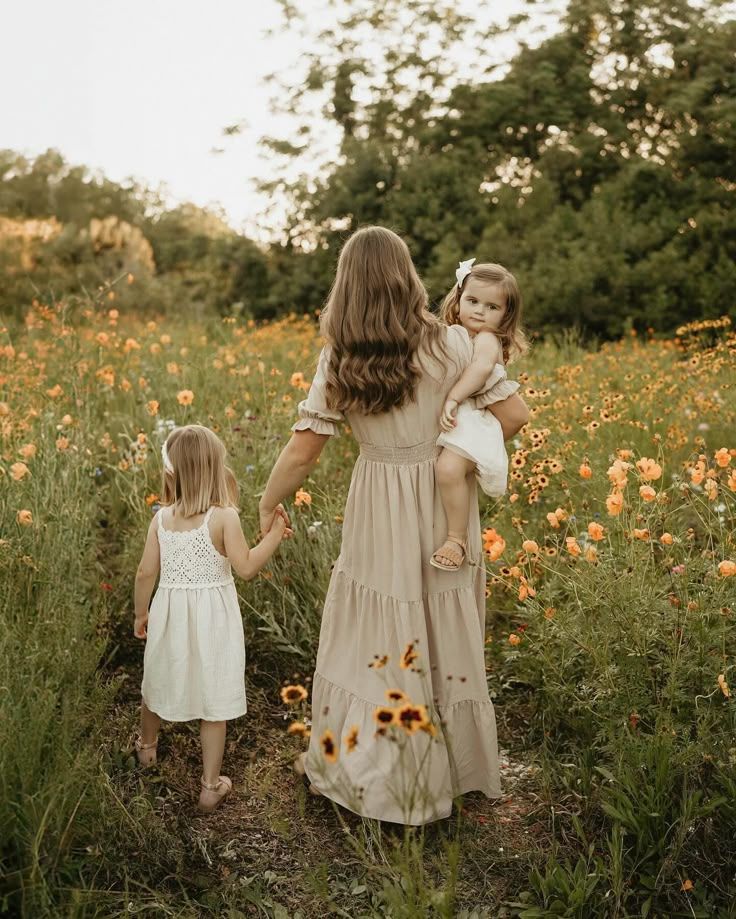 Two children in brown and orange dresses sitting together in tall golden grass with evergreen trees in background.