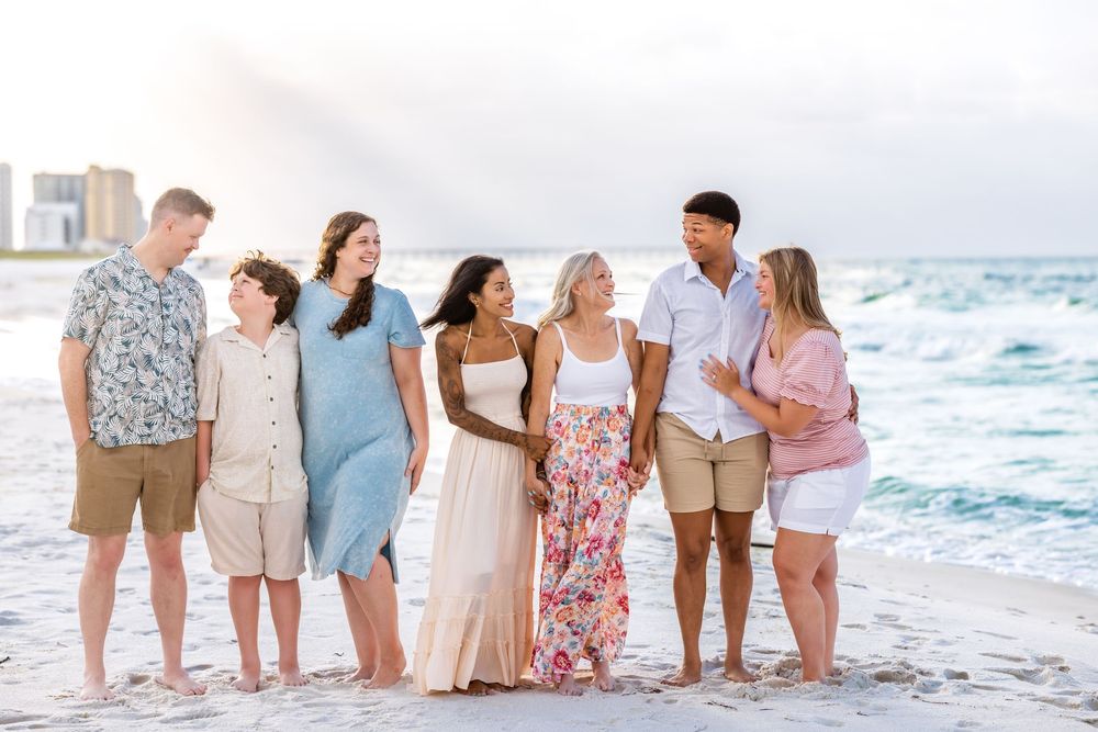 People in coordinating outfits standing together on a sandy beach at sunset with ocean waves in the background.