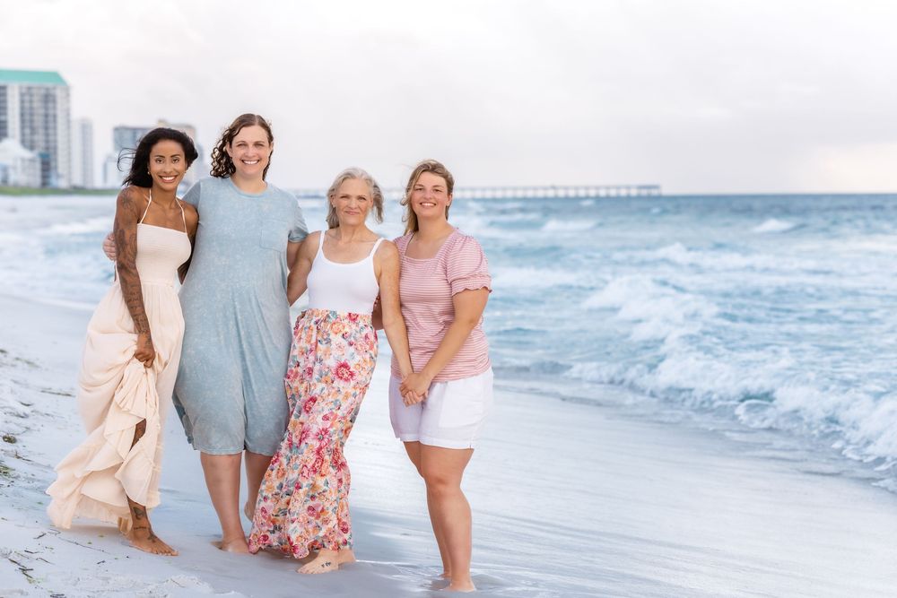A group in coordinated outfits walks along a sandy beach at sunset with waves crashing in the background.