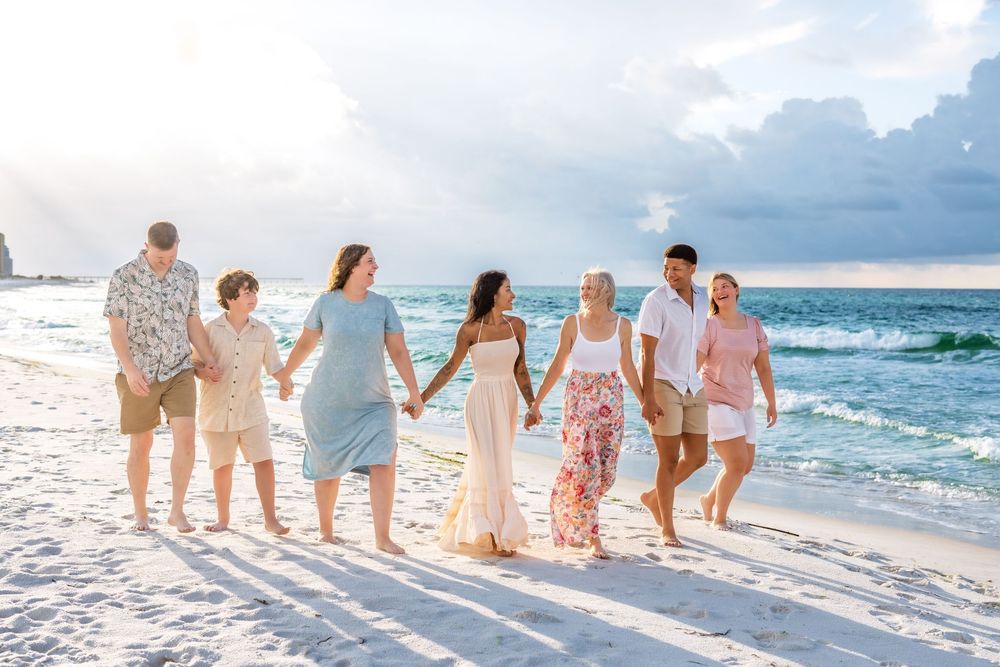 A group walks together along a white sandy beach at sunset with ocean waves and cloudy sky in view.