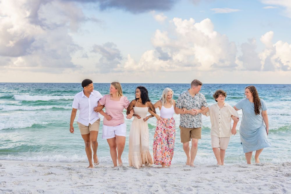 Group walking together on a white sandy beach at sunset with turquoise ocean waves and cloudy sky in background.