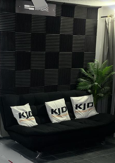 Empty recording studio with black acoustic panels and white cushions on a black couch against the wall.