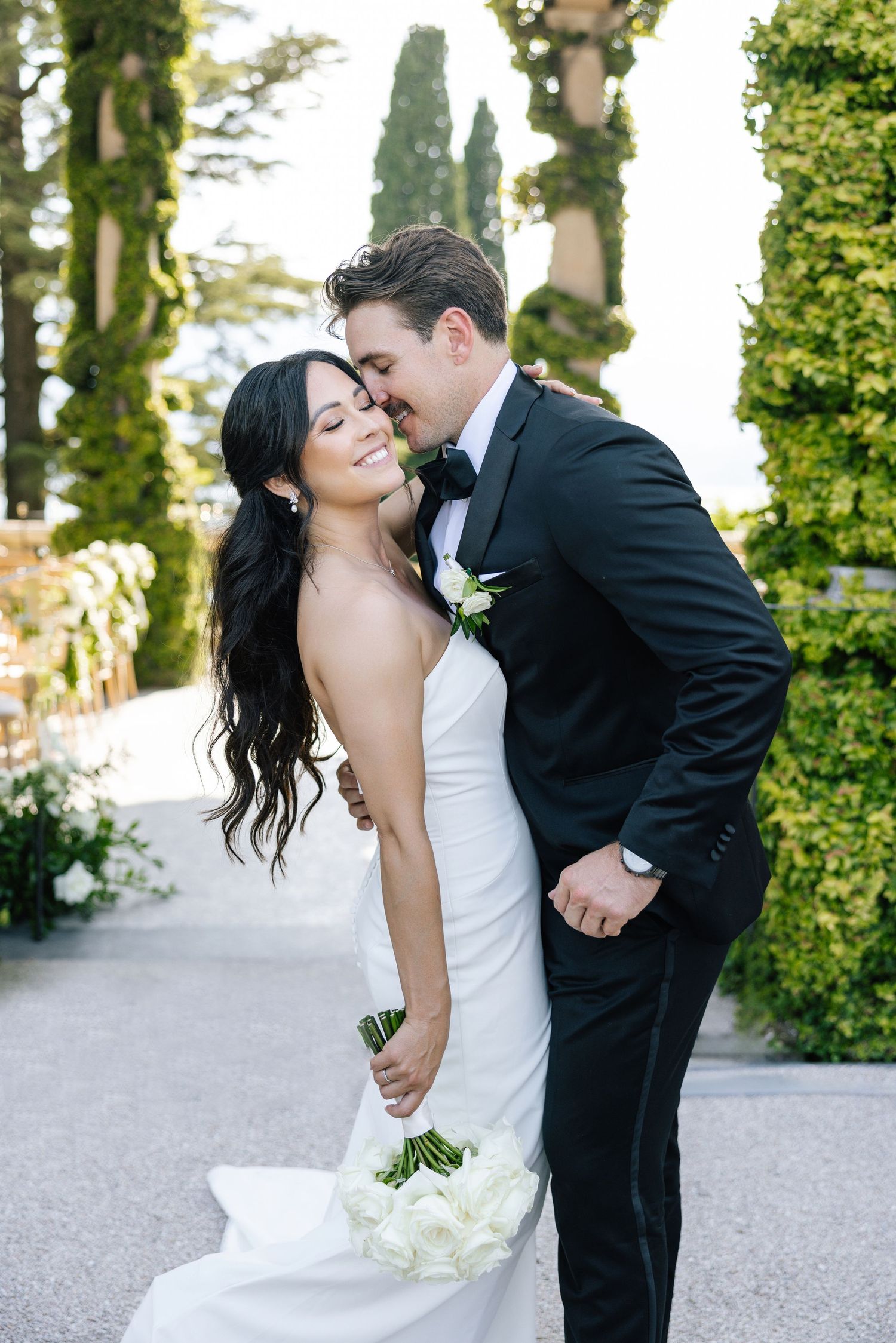 Bride in flowing white gown poses near fountain outside French chateau.