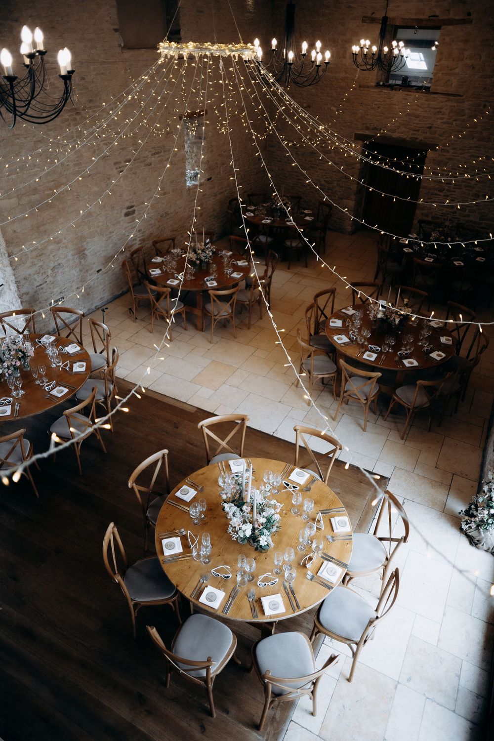 Overhead view of elegant wedding reception tables with round settings, wooden chairs, and twinkling string lights above.