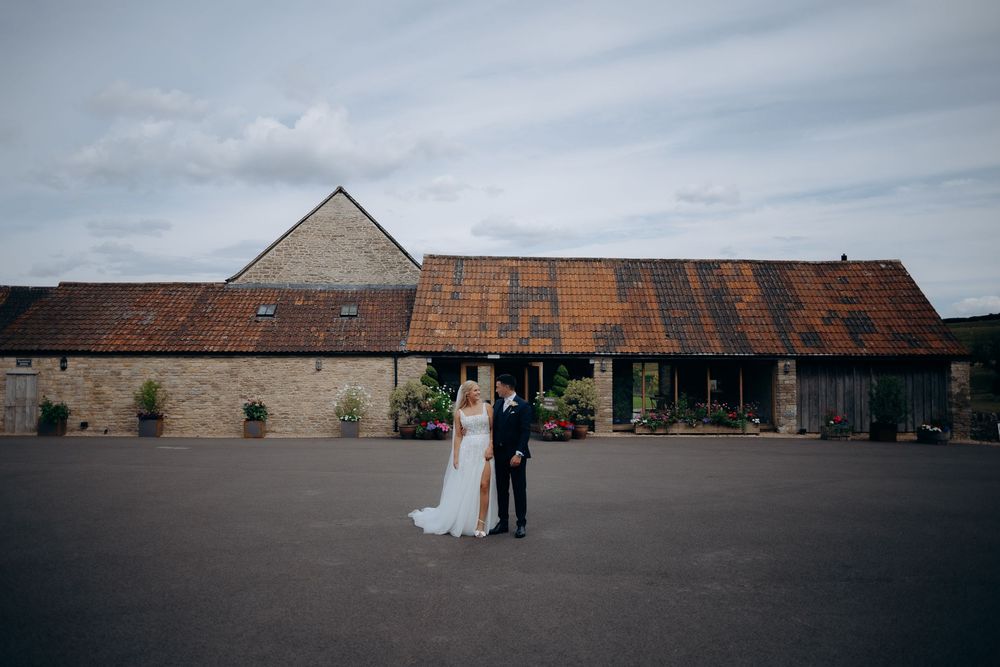 Rustic stone barn venue with red roof tiles serves as backdrop for a wedding ceremony on an overcast day.