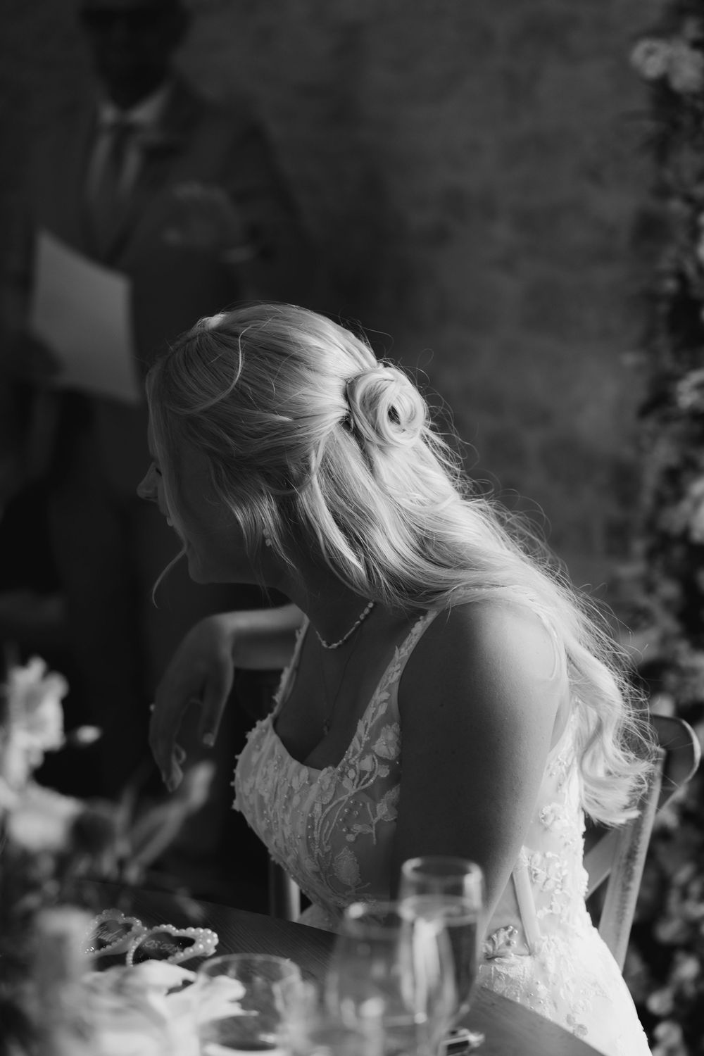 Black and white wedding photo showing a lace dress and elegant updo hairstyle at a reception table.