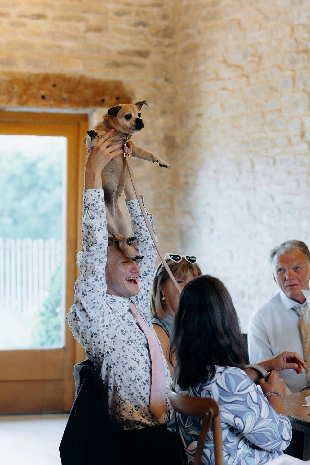 Small dog being held up high during a joyful celebration moment at an indoor event.