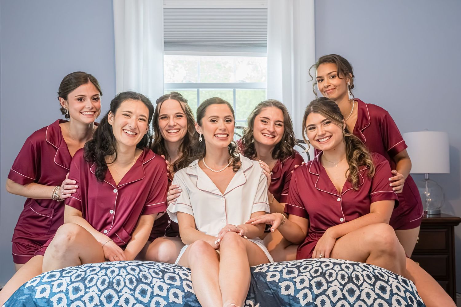 Group in burgundy robes and white dress sitting together on blue patterned bedding while sharing joyful moment.