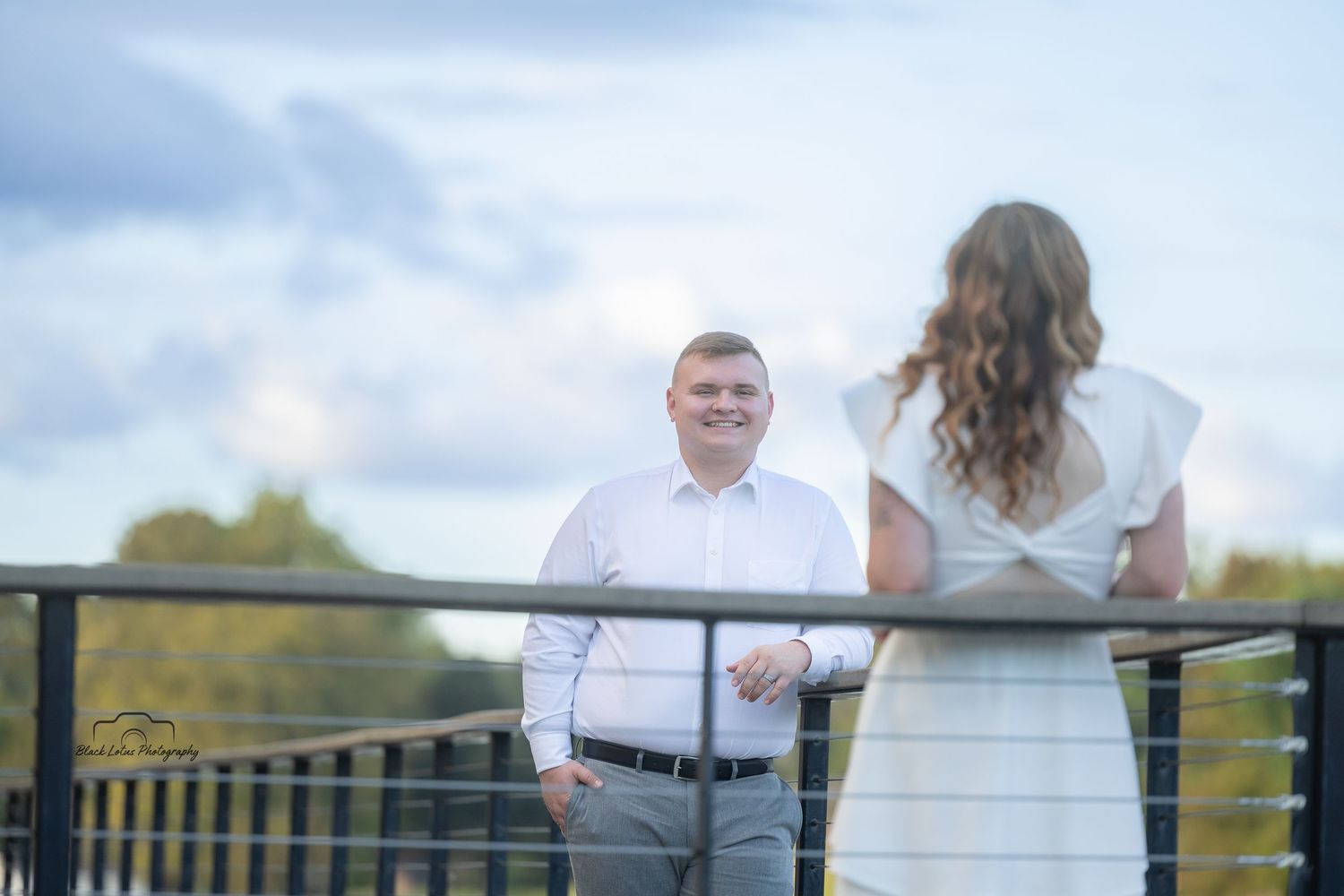 A couple in wedding attire stands together on a wooden deck overlooking a scenic landscape on their special day.