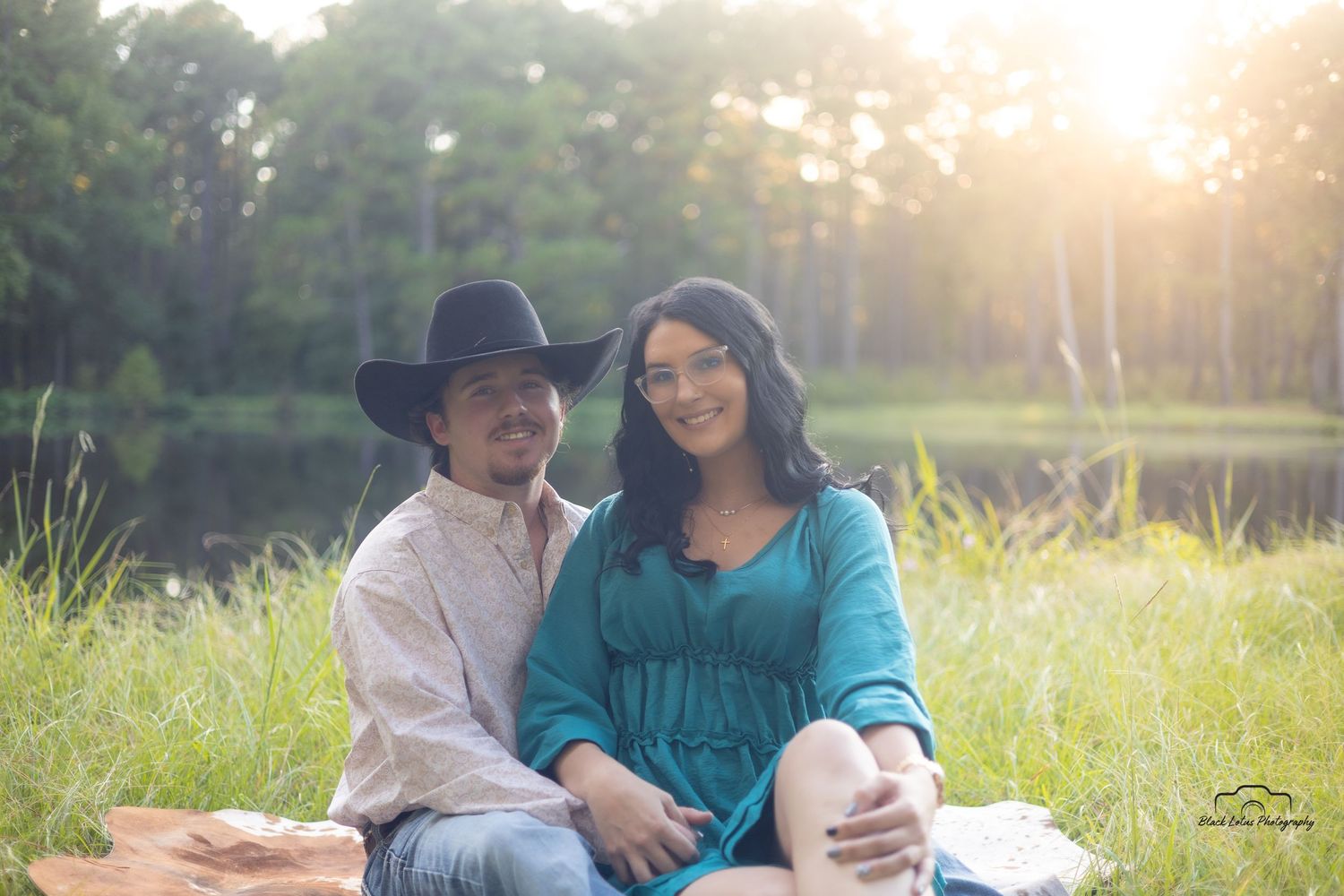 A couple sits together in a sunlit meadow wearing coordinating outfits of denim and turquoise during golden hour.