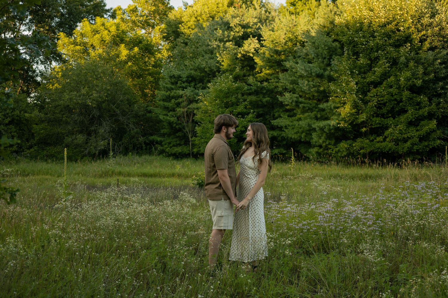 A couple plays and spins in a flower and grass field during their engagement photos in Flushing, Michigan.