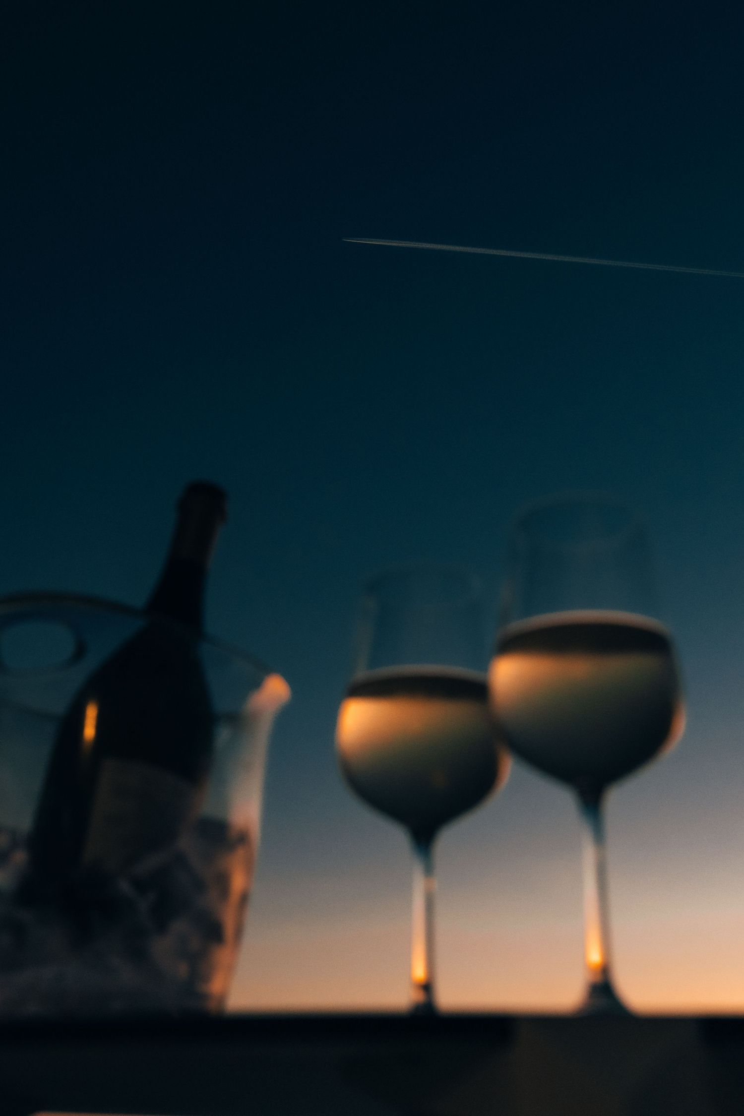 Silhouetted wine glasses and bottle against a dusky evening sky with a contrail visible. Mtlshutter photography