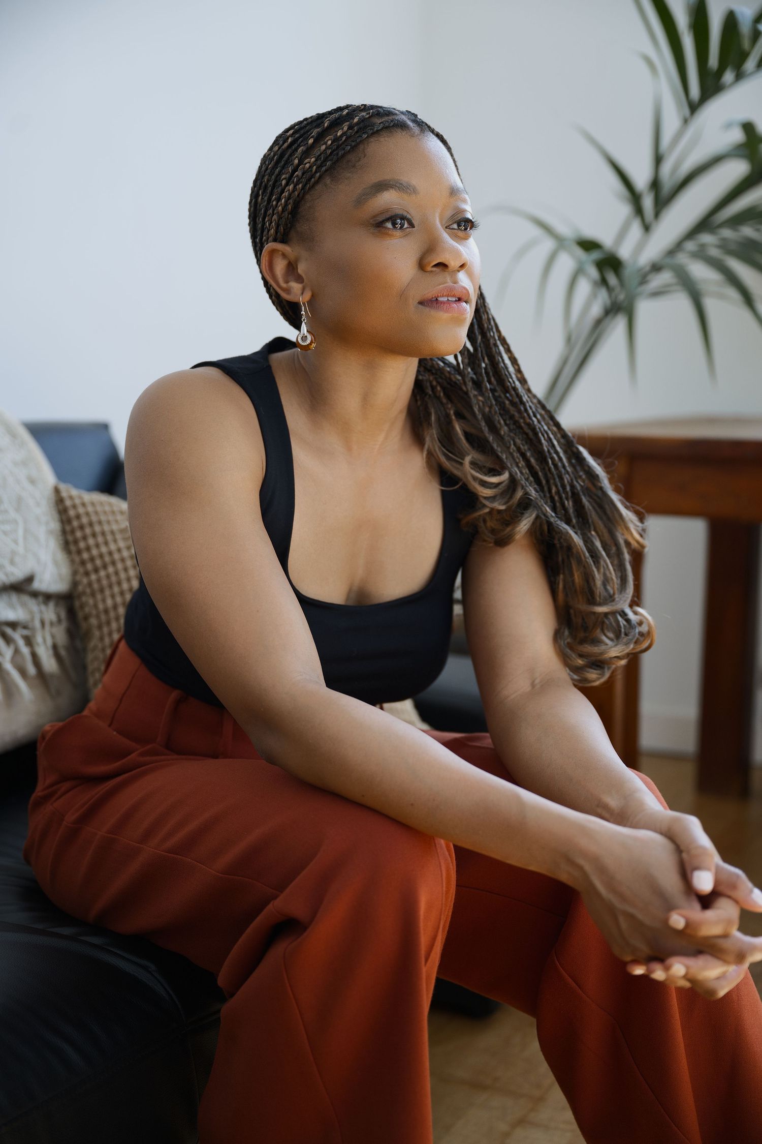 Casual indoor portrait showing relaxed pose in black tank top and rust-colored pants.