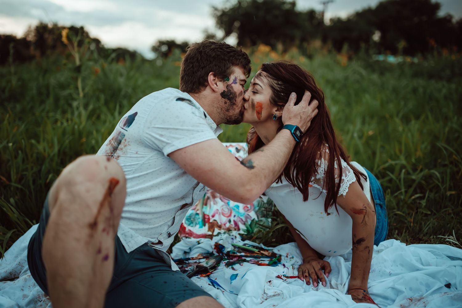 An intimate couple sharing a romantic moment on a picnic blanket in a grassy meadow at sunset.