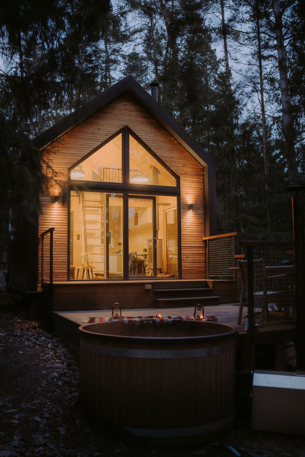 Modern A-frame cabin with glass facade and outdoor hot tub glowing warmly in dark forest.