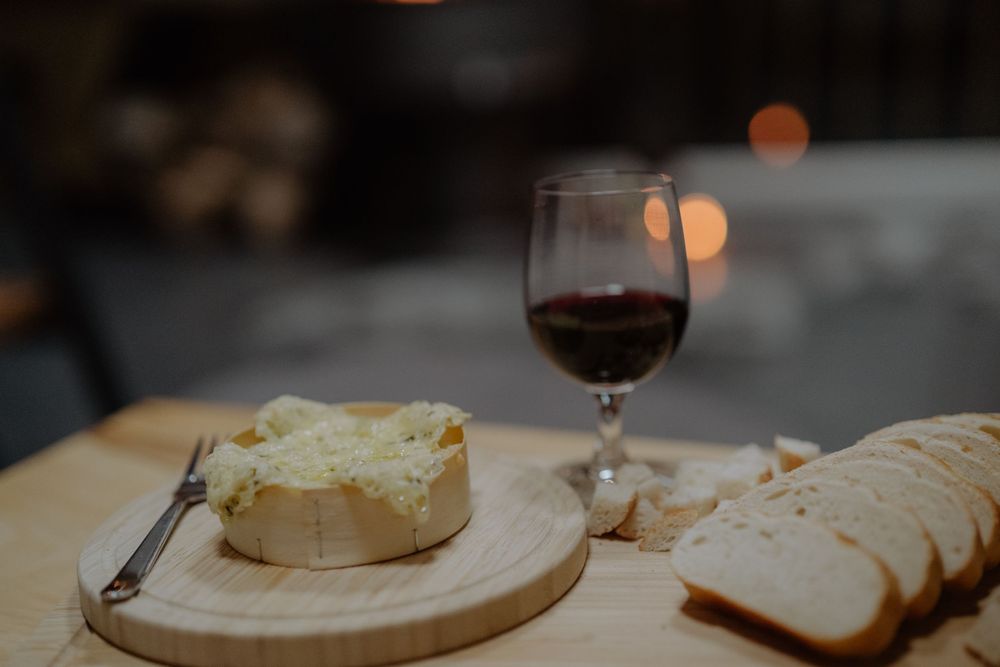 Wine glass and sliced bread on wooden board in dim lighting setting.