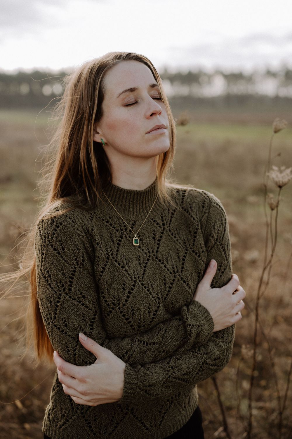 Person in cozy sweater embraces themselves while standing in golden autumn field.