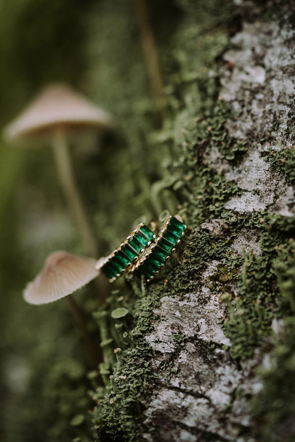 Emerald green stud earrings displayed on tree bark with mushrooms in background.