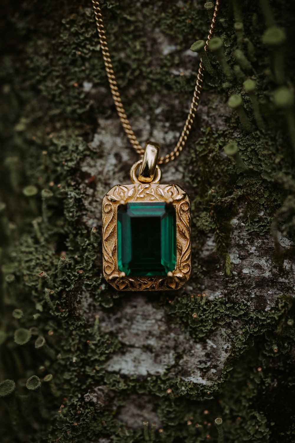 Vintage gold and emerald pendant necklace displayed on mossy tree bark.