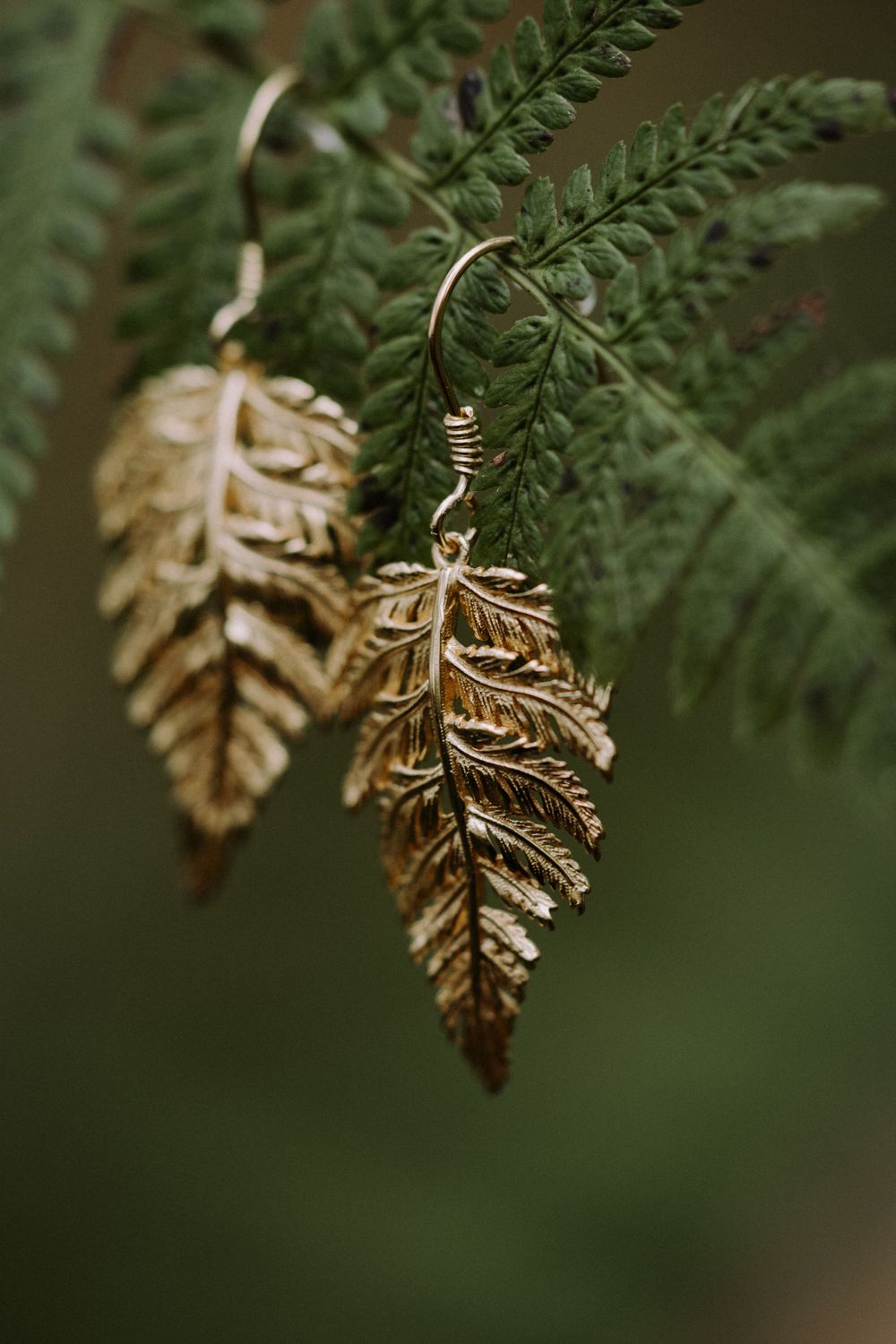 Detailed shot of gold fern leaf earrings hanging against green ferns.