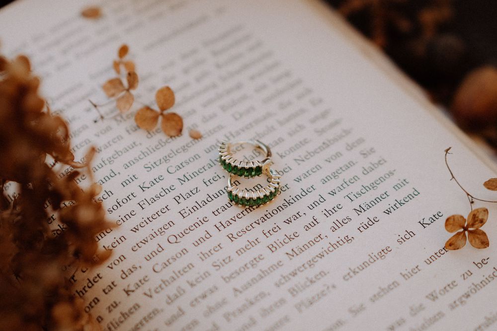 Wedding rings rest on open book pages with dried flowers creating romantic composition.