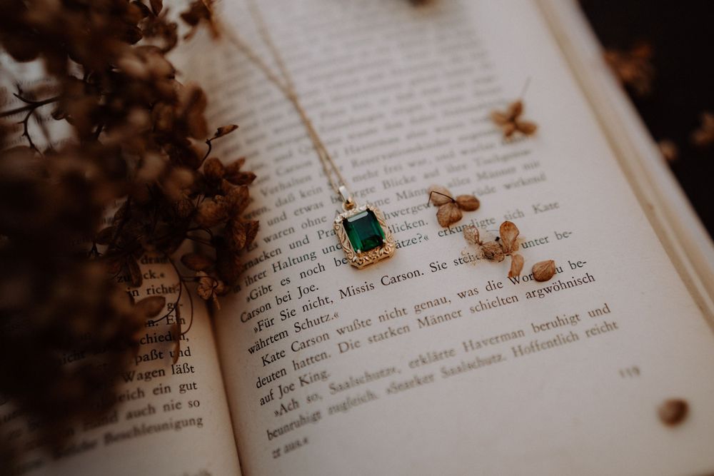Emerald necklace pendant placed on vintage book pages with dried botanical elements.
