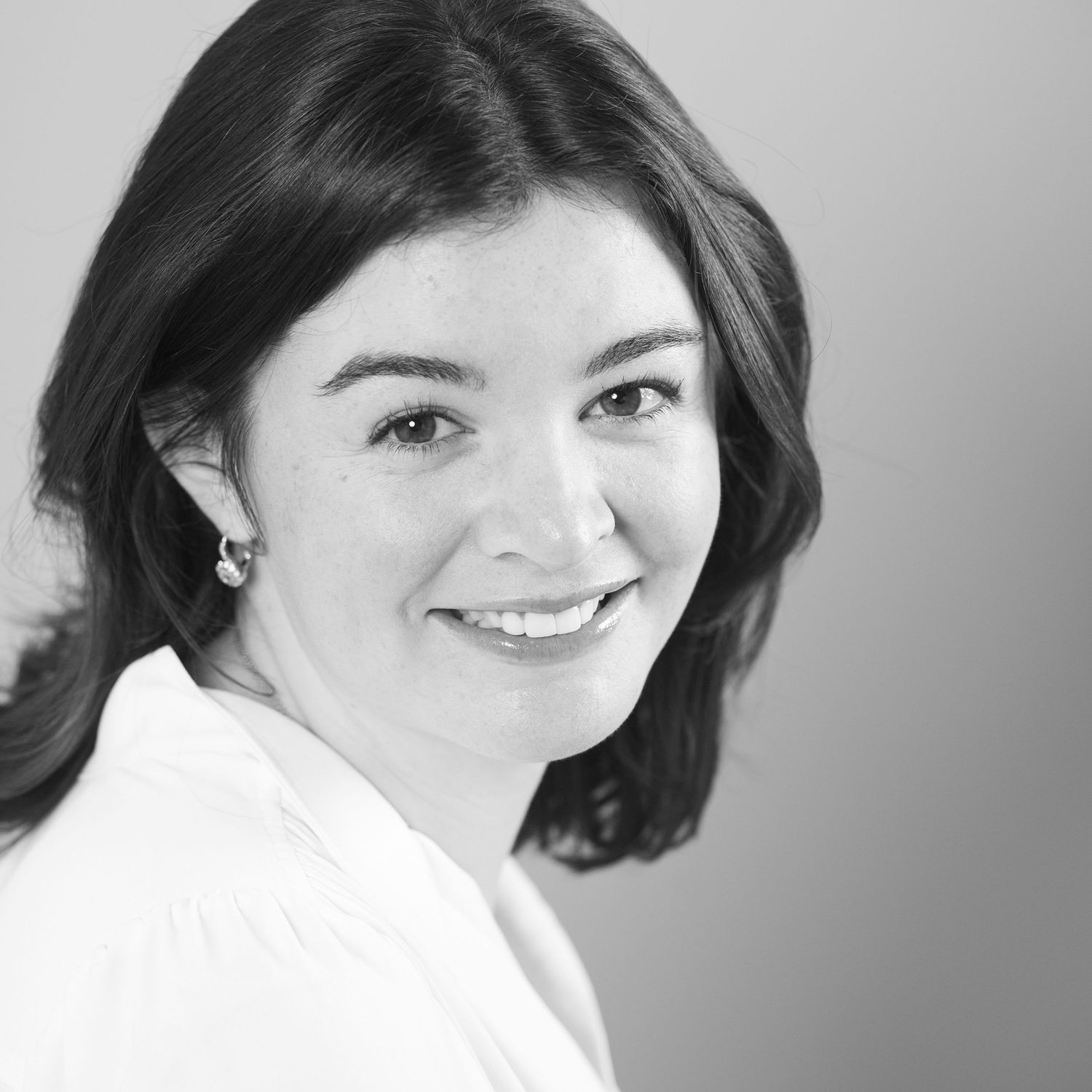 Black and white professional headshot of a smiling woman with dark hair wearing a white top.
