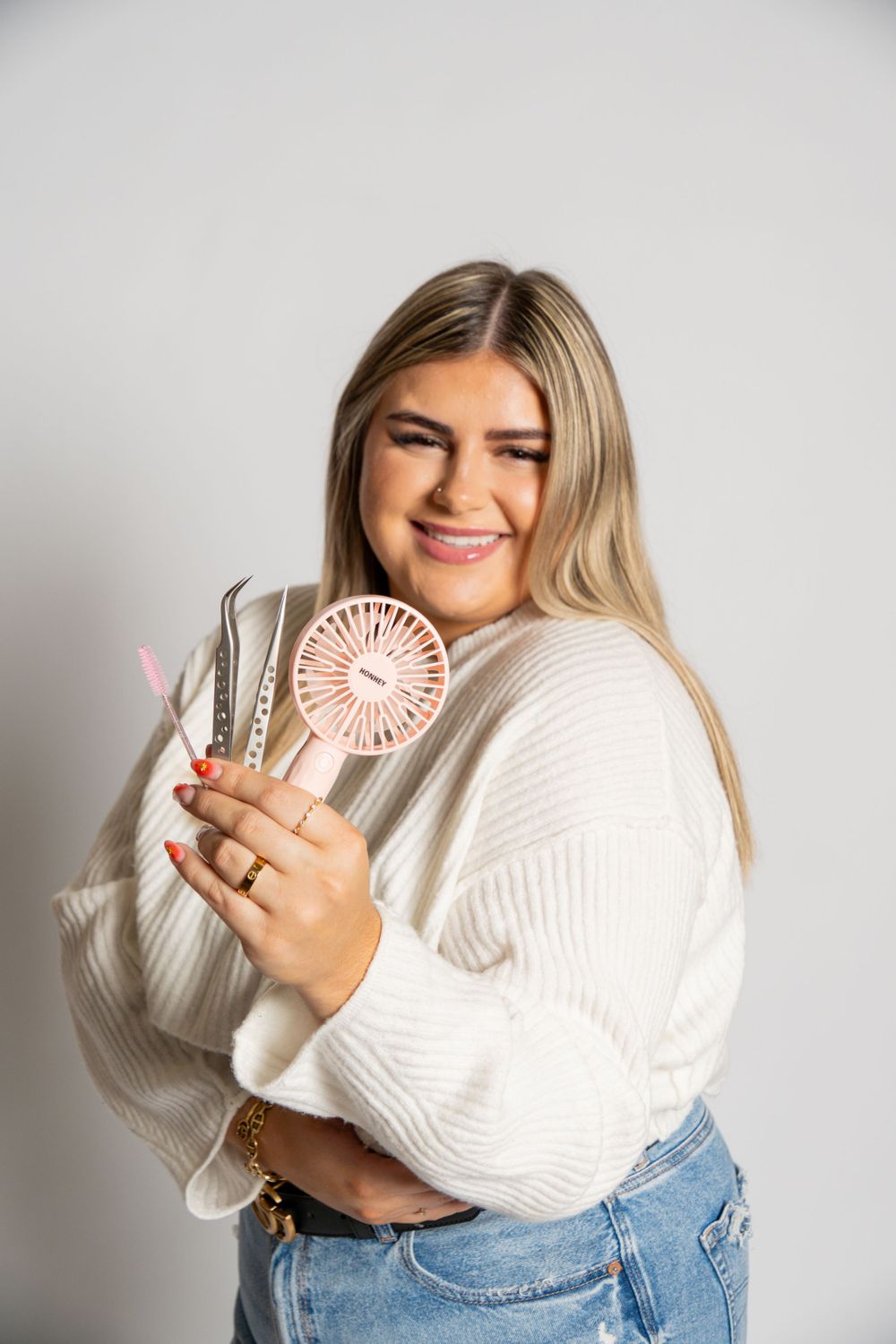 Studio portrait holding a pink handheld fan while wearing a white sweater and jeans.