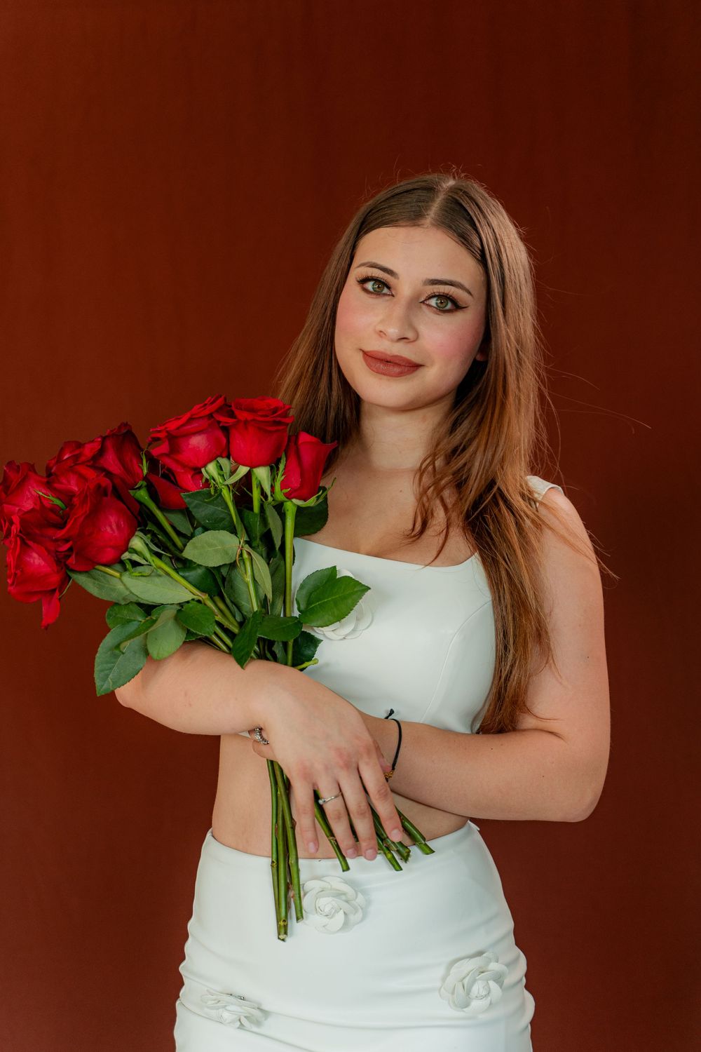 Woman in white dress holding beautiful bouquet of red roses against burgundy background.