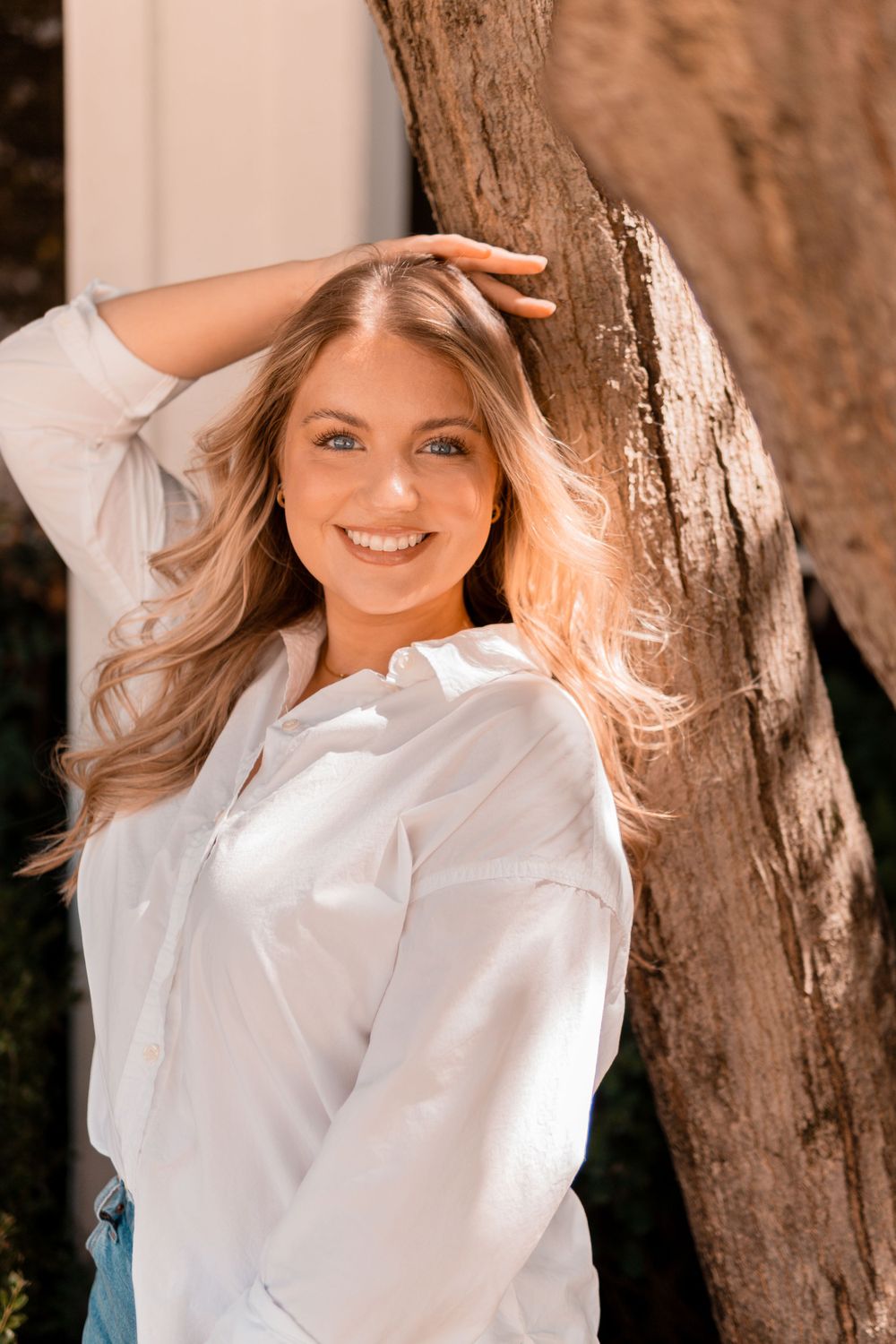 Portrait against a tree trunk showing a white button-down shirt in warm sunlight.