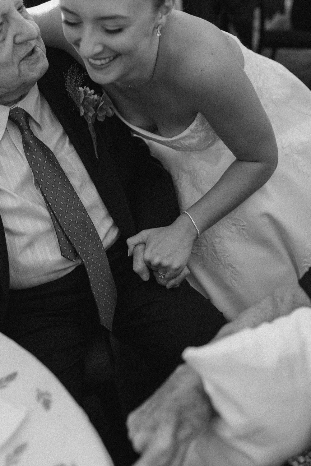 Black and white photo of a smiling bride in a wedding gown holding hands with an elderly man in a suit.