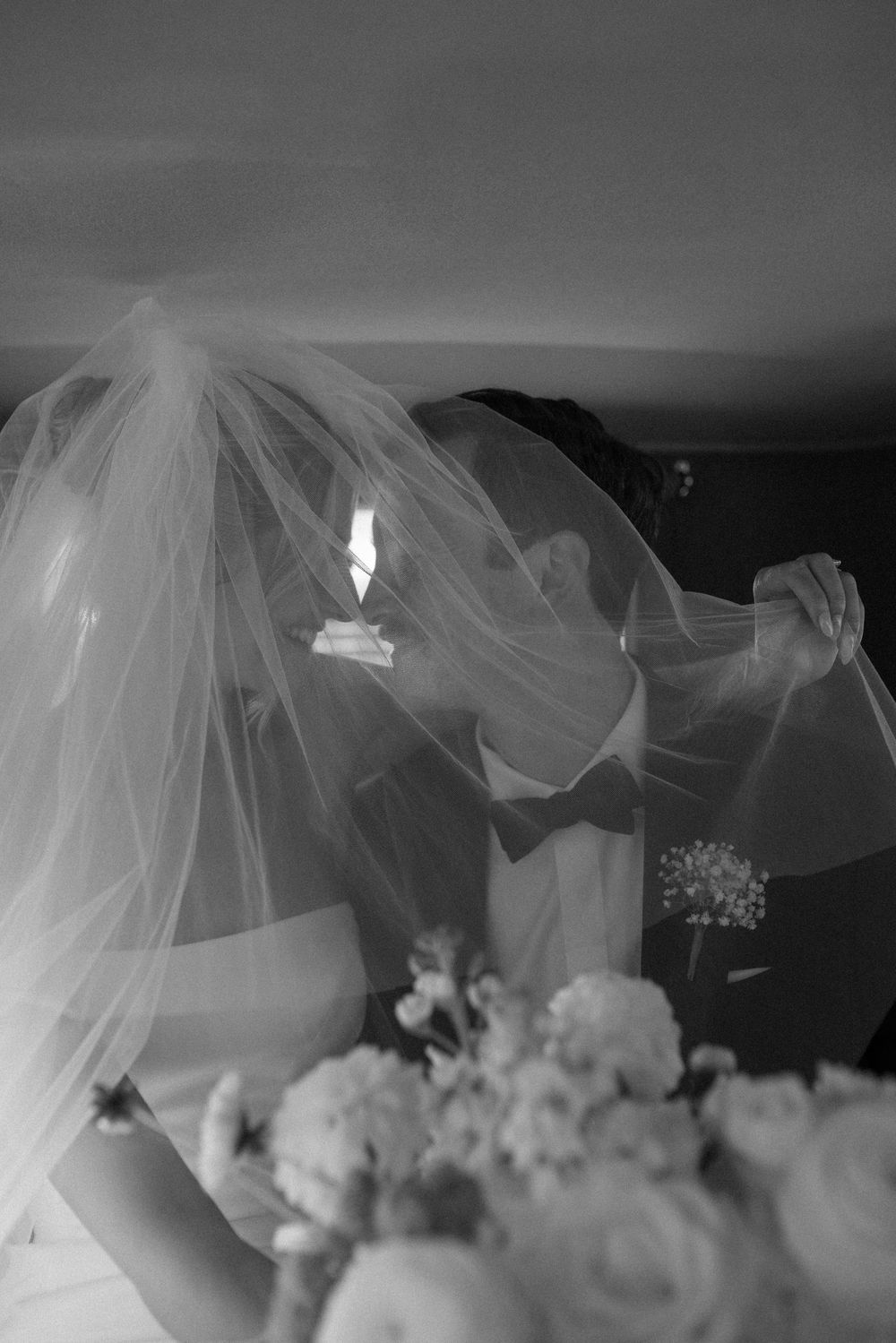 A flowing white wedding veil billows dramatically in black and white against a dark background.