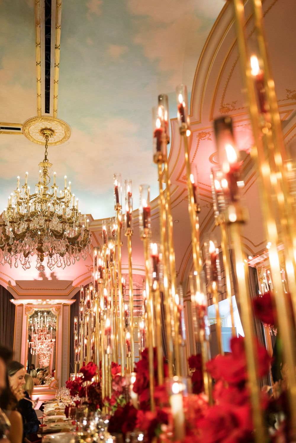 Elegant ballroom with gold candelabras, red roses, crystal chandelier, and painted ceiling at a luxury event.
