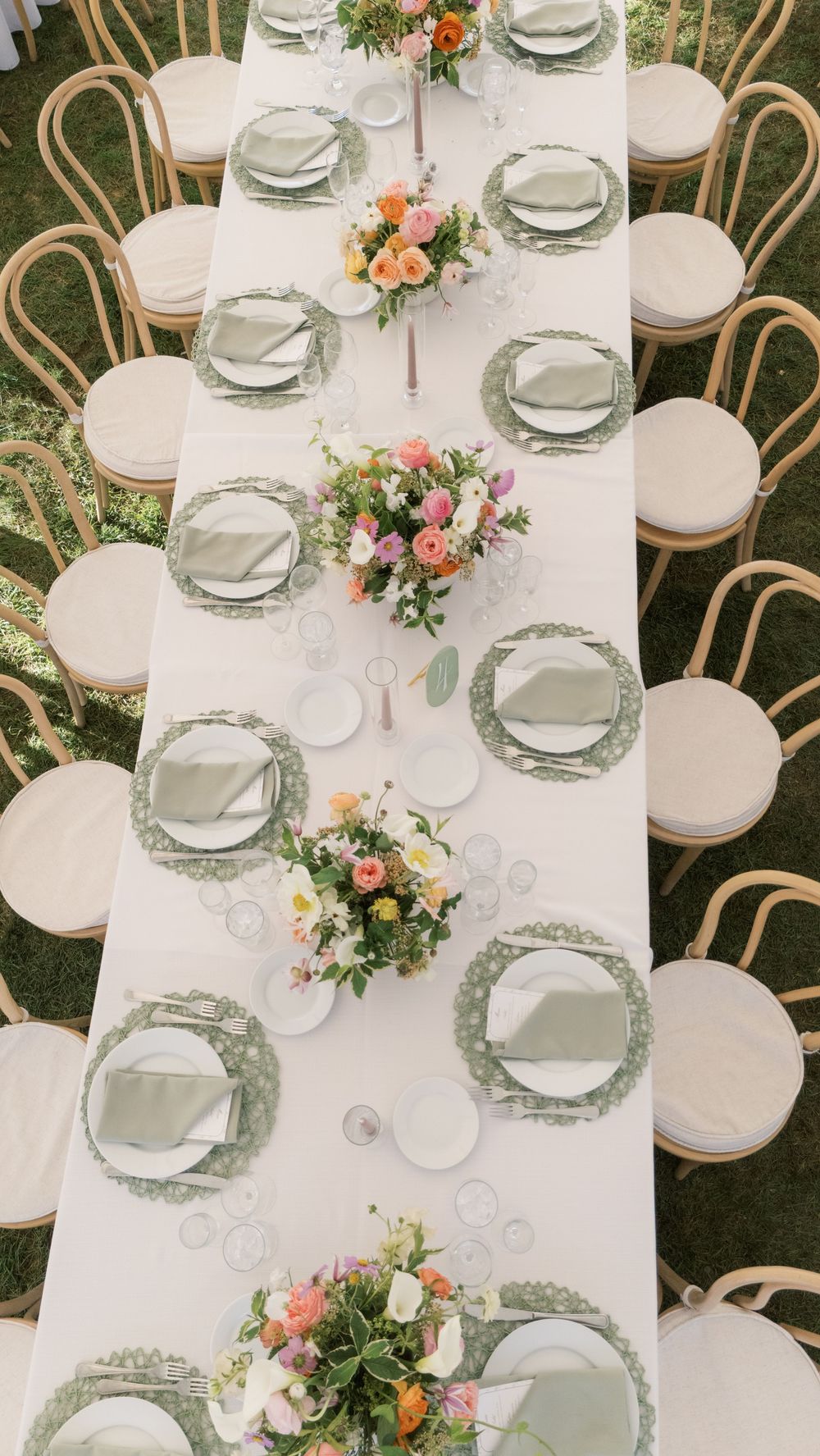 Aerial view of elegant outdoor wedding reception table with sage green chargers, white linens, and colorful floral centerpieces.