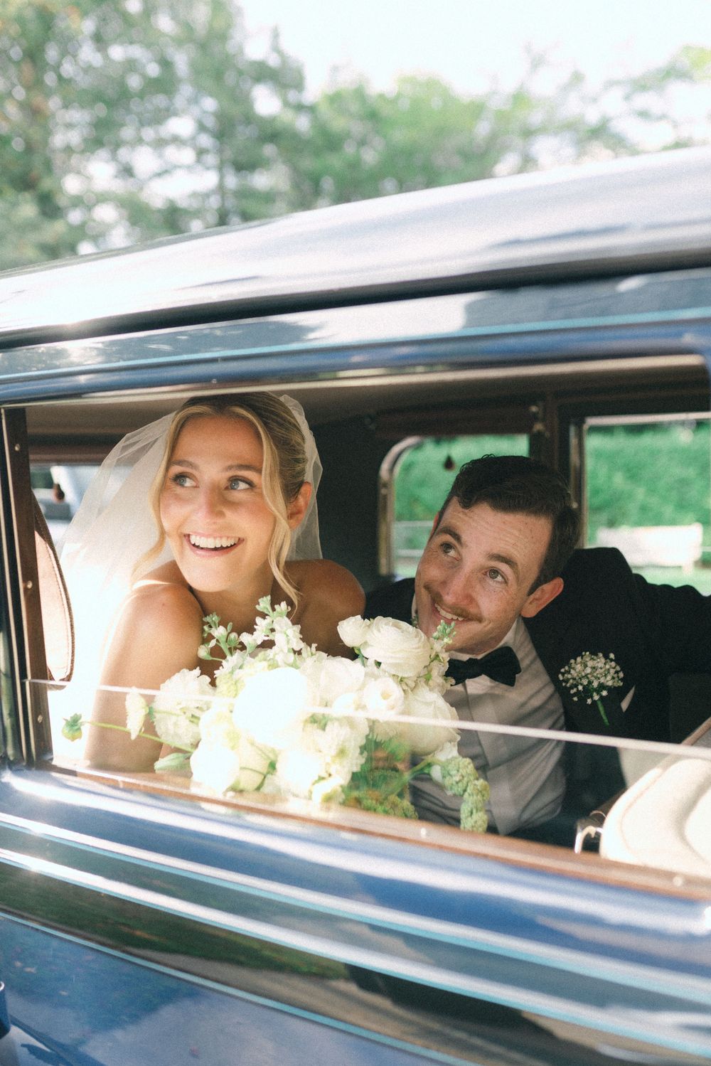 A happy couple shares joyful moments together while sitting in a classic car on their special day.