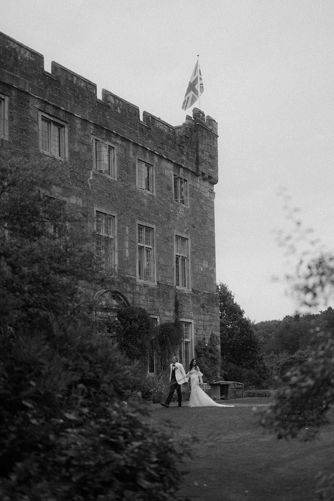 A couple in wedding attire walking in front of a Askham Hall, captured in dramatic black and white by Lincolnshire photographers.