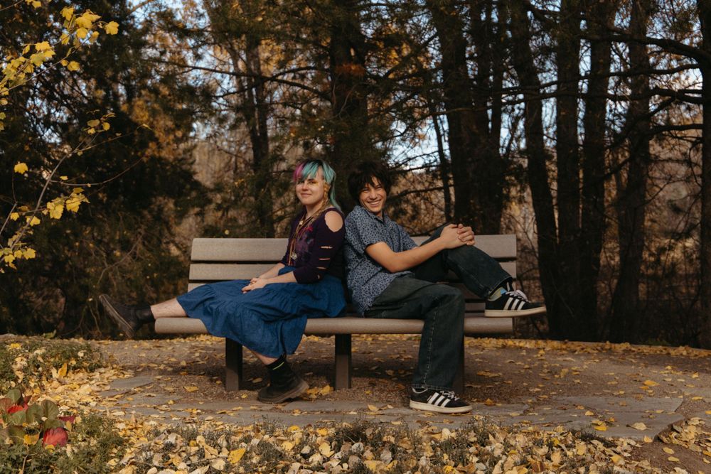Family members relaxing on a wooden bench surrounded by fallen autumn leaves.
