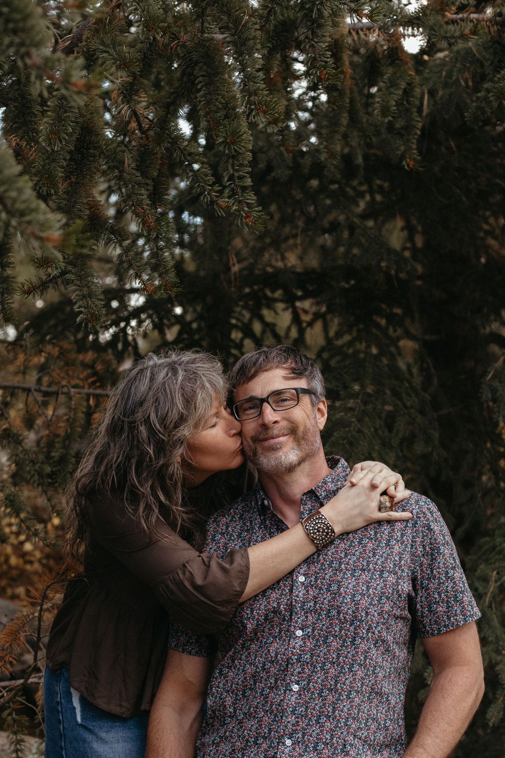 A couple shares an intimate moment against a backdrop of evergreen trees.