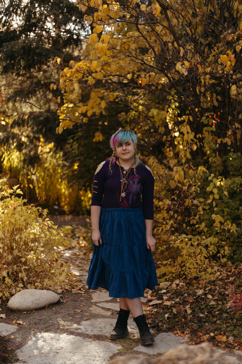 Person wearing a navy dress stands on a path surrounded by vibrant yellow fall foliage.