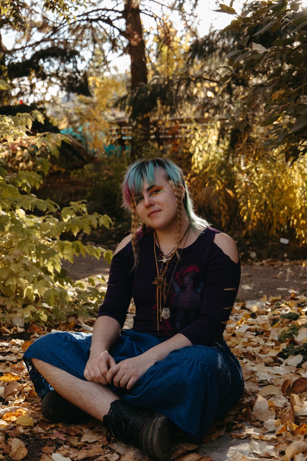 Figure relaxes on ground covered in autumn leaves during golden hour lighting.