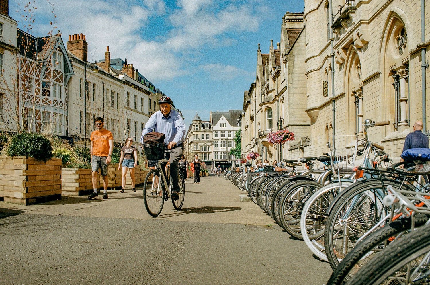 Row of parked bicycles along historic Oxford street with classical architecture and pedestrians.